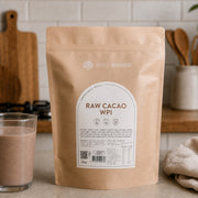 Bare Blends Raw Cacao WPI 750g pouch beside a chocolate protein shake in a kitchen